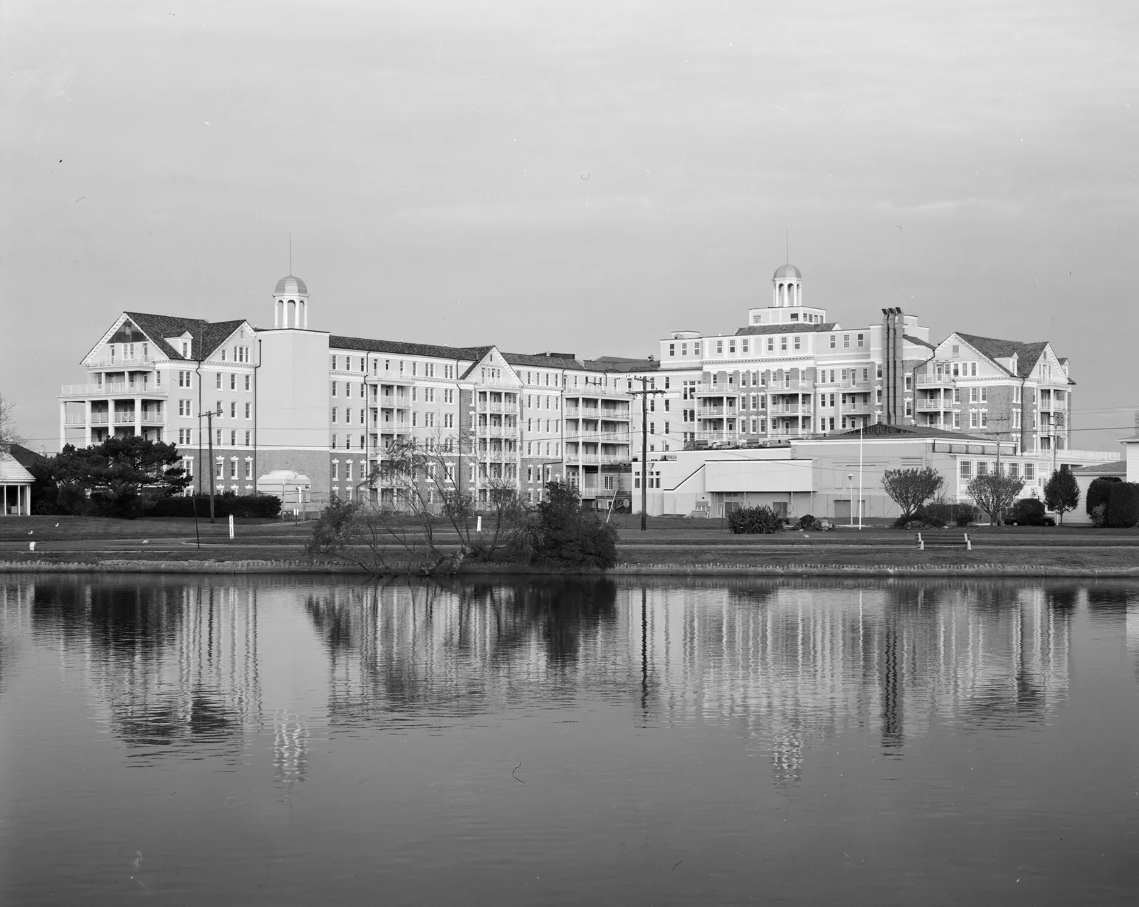 Black and white photo of the long white Essex and Sussex Hotel reflected in the lake