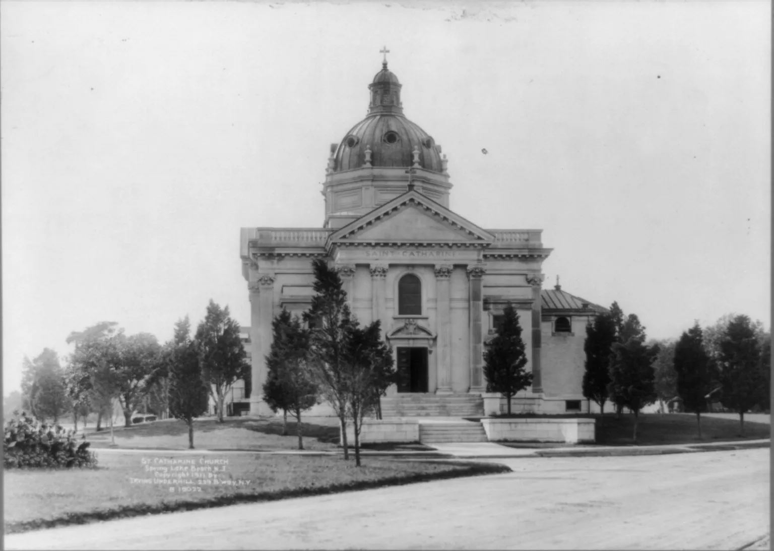 Black-and-white photo of a domed classical church with columns and young trees along its lawn