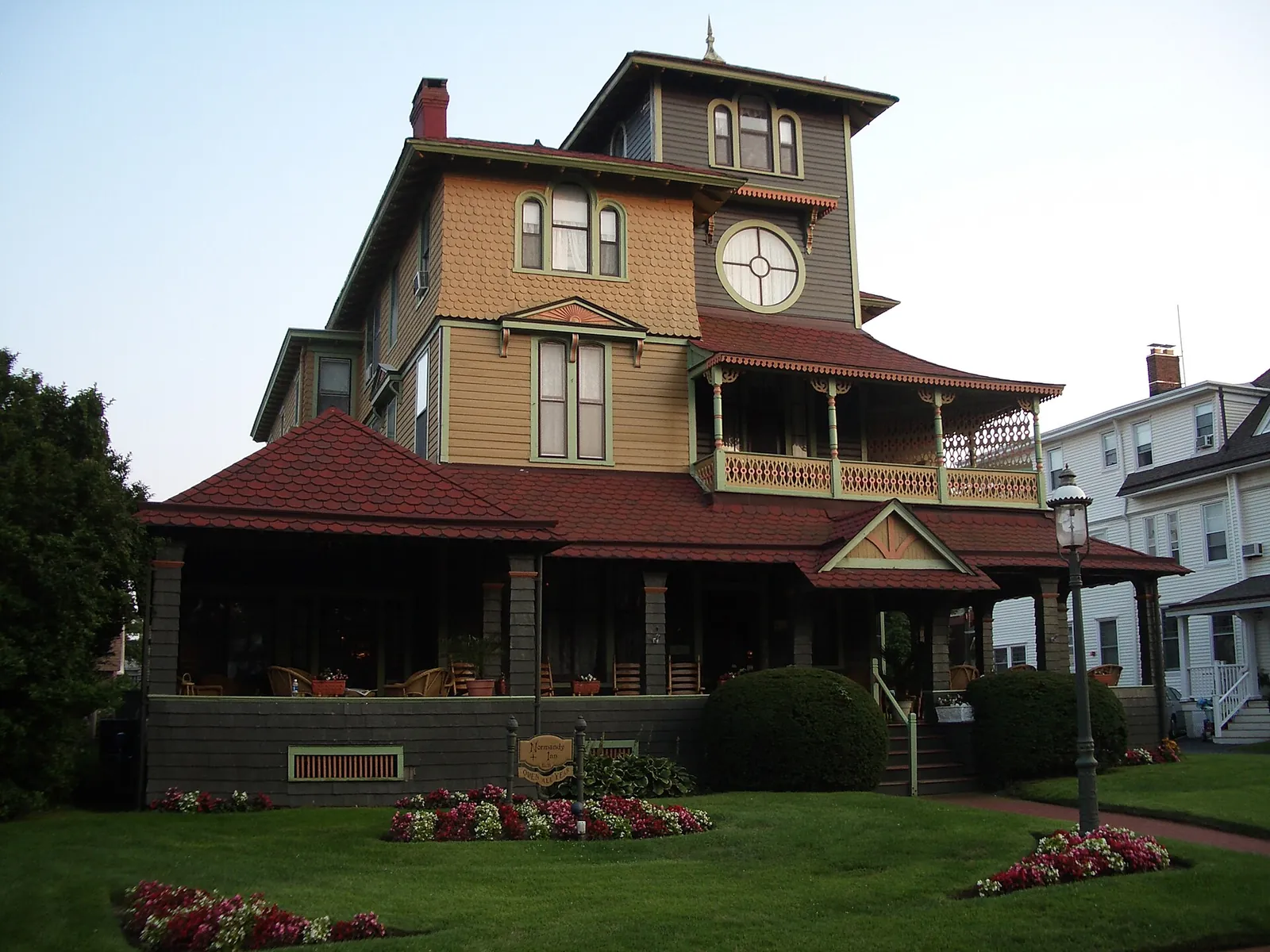 A Victorian house with a tall tower, a round clock-face window and a red roof over a deep porch