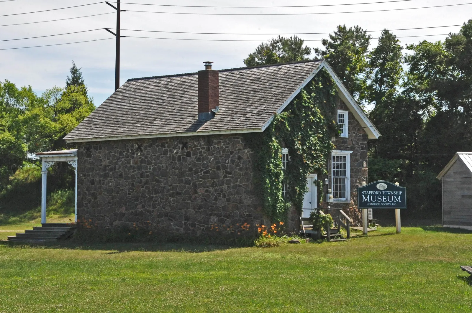 A small stone building with ivy on one wall and a museum sign on the lawn in front