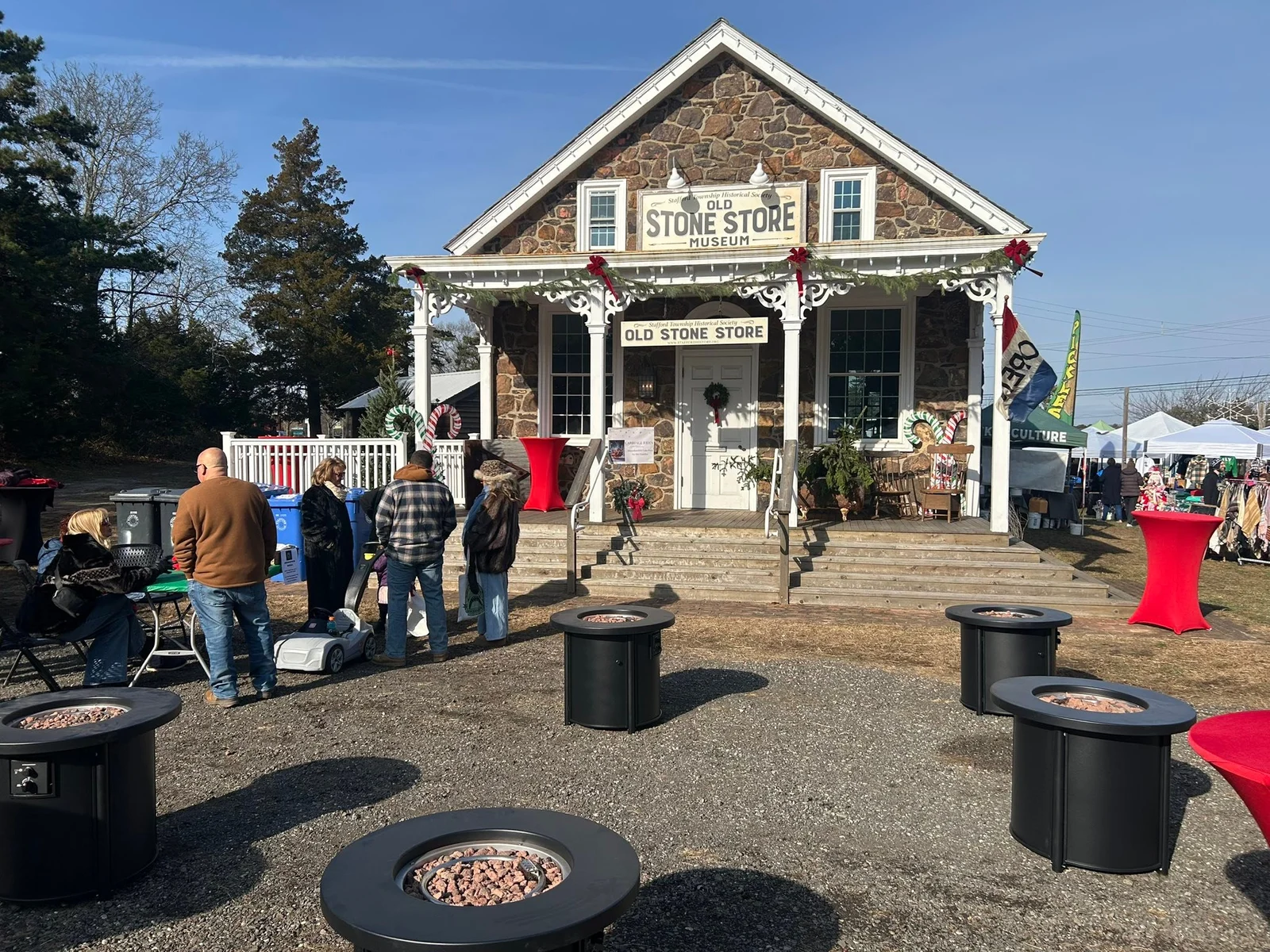 The Old Stone Store decorated with garland for Holiday Wonderland, with fire pits and visitors on a sunny December day
