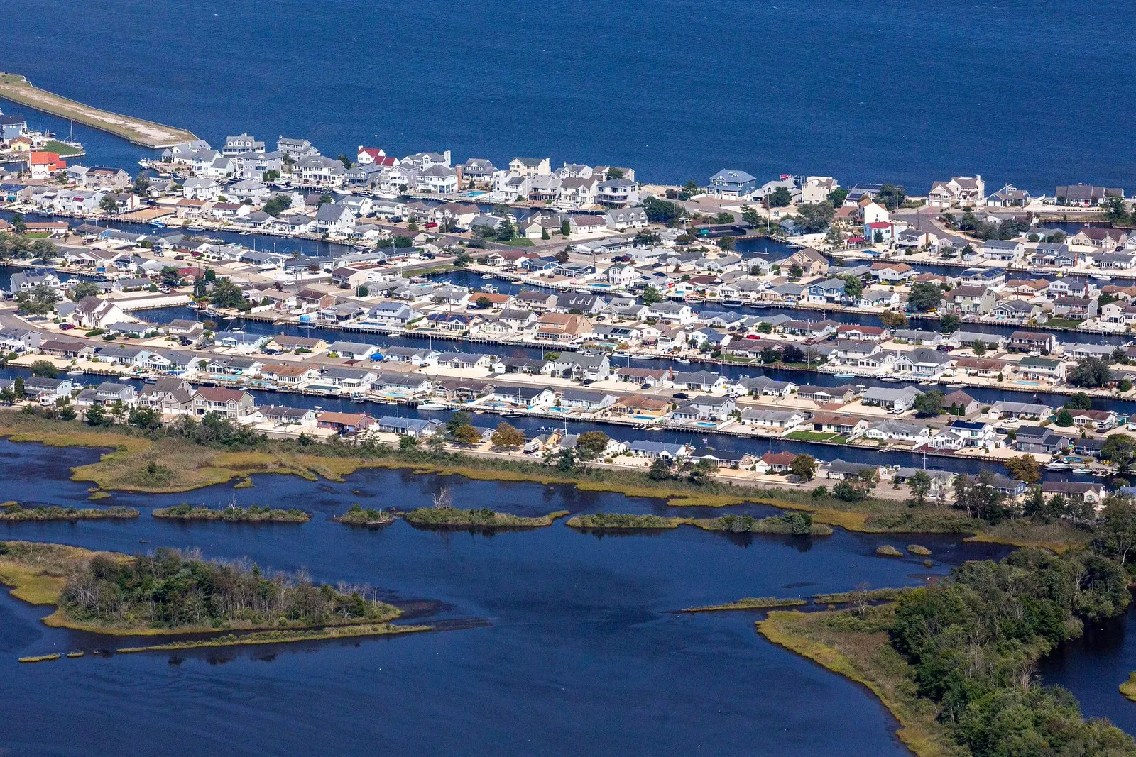 Aerial view of waterfront streets and lagoons beside open bay water and green marsh islands