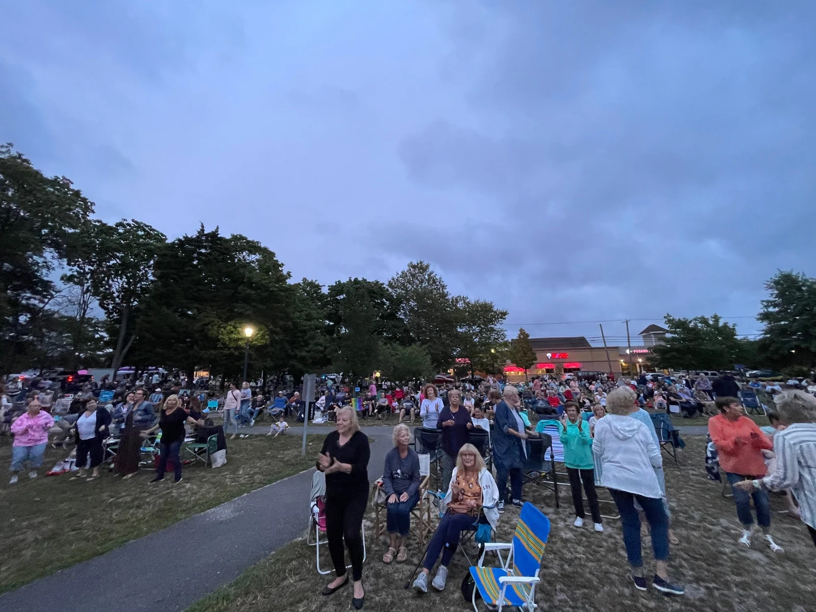 A large crowd with lawn chairs on the grass at Manahawkin Lake Park for an evening summer concert