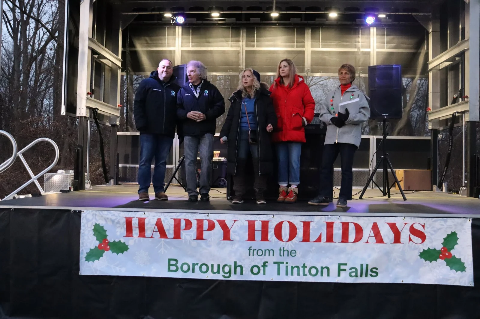 Borough officials on an outdoor stage hung with a Happy Holidays from the Borough of Tinton Falls banner