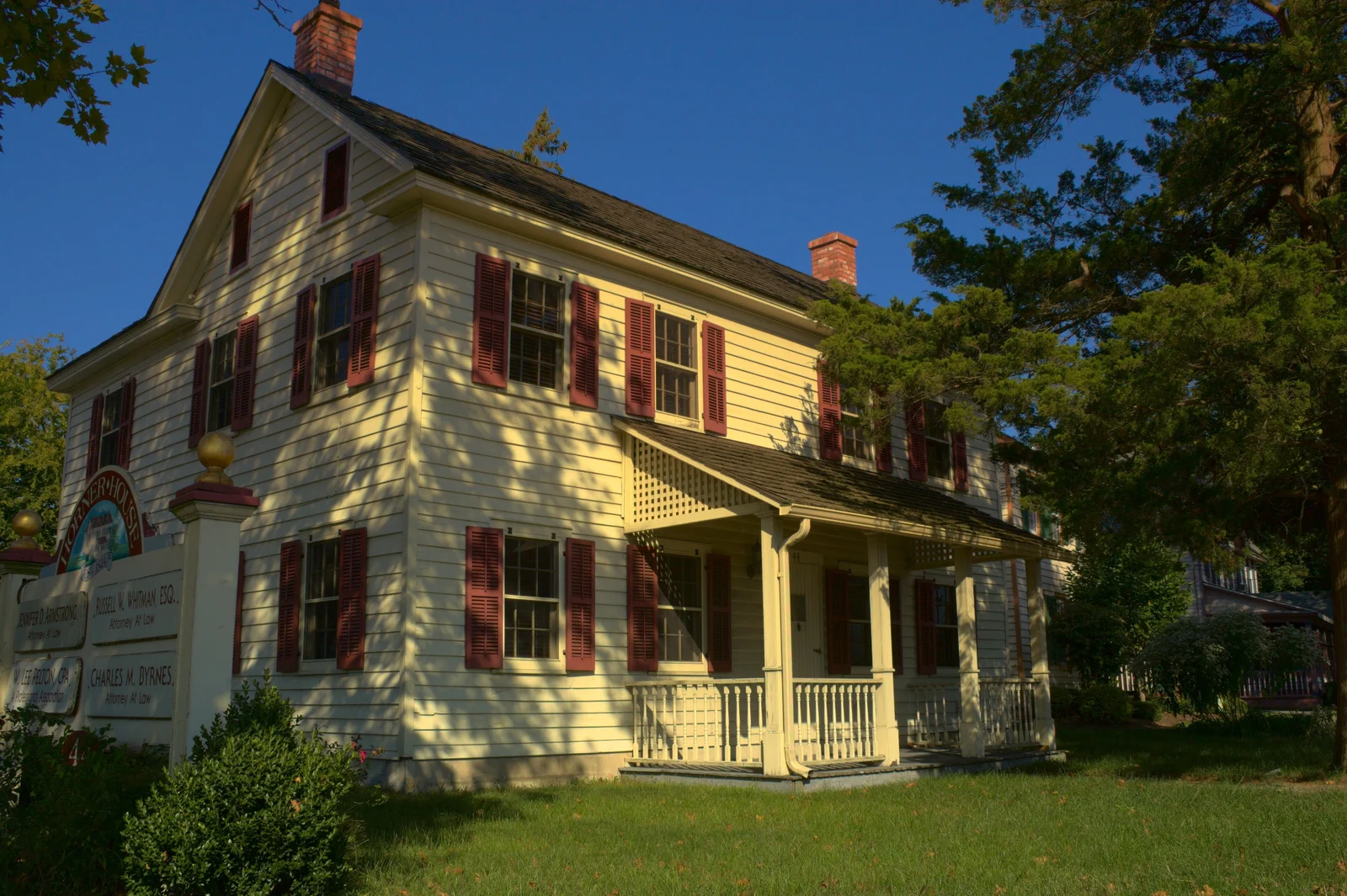 Pale yellow two-story house with red shutters and a front porch behind a green lawn