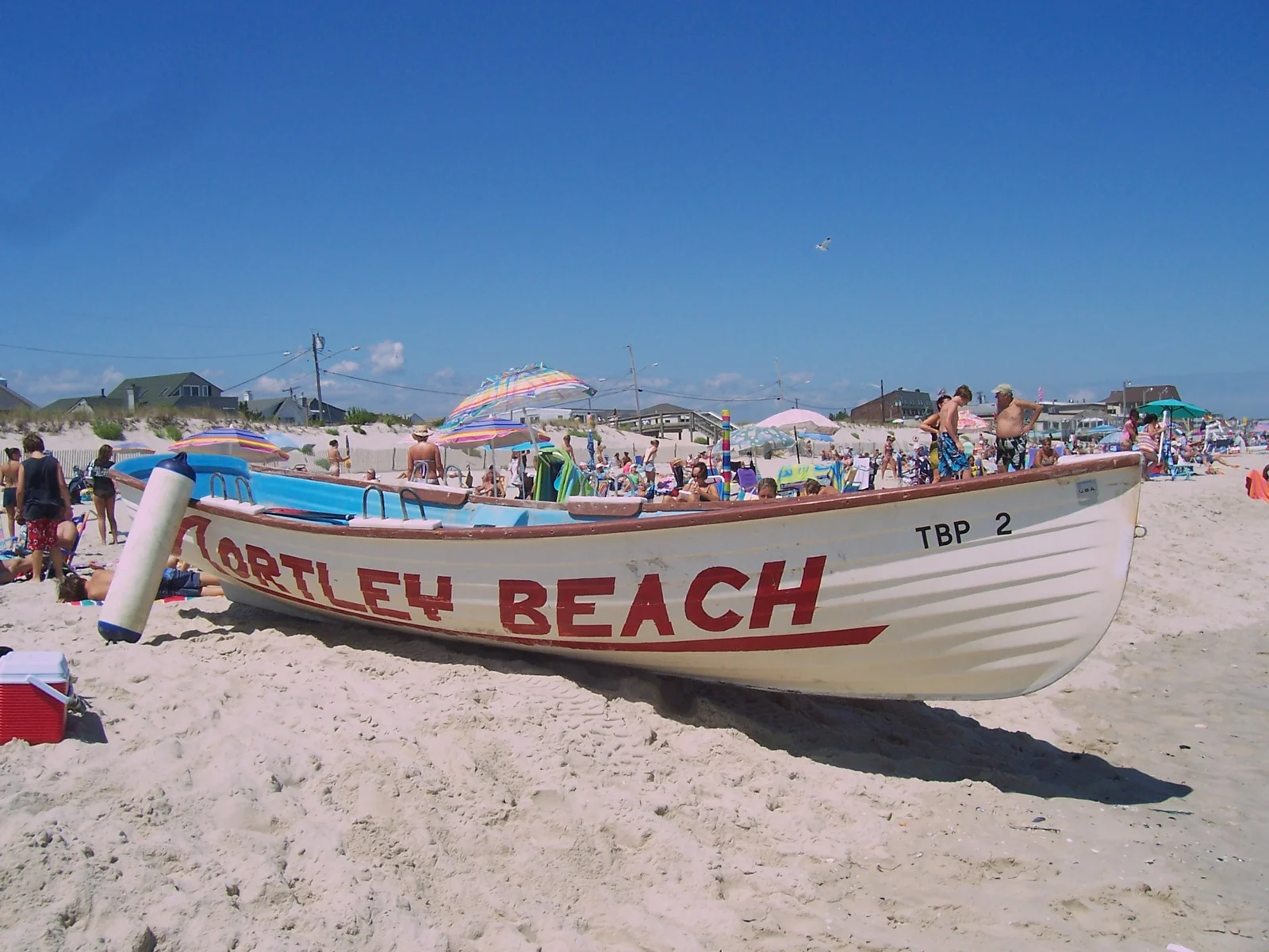 A white Ortley Beach lifeguard boat on the sand in front of a busy summer beach with umbrellas