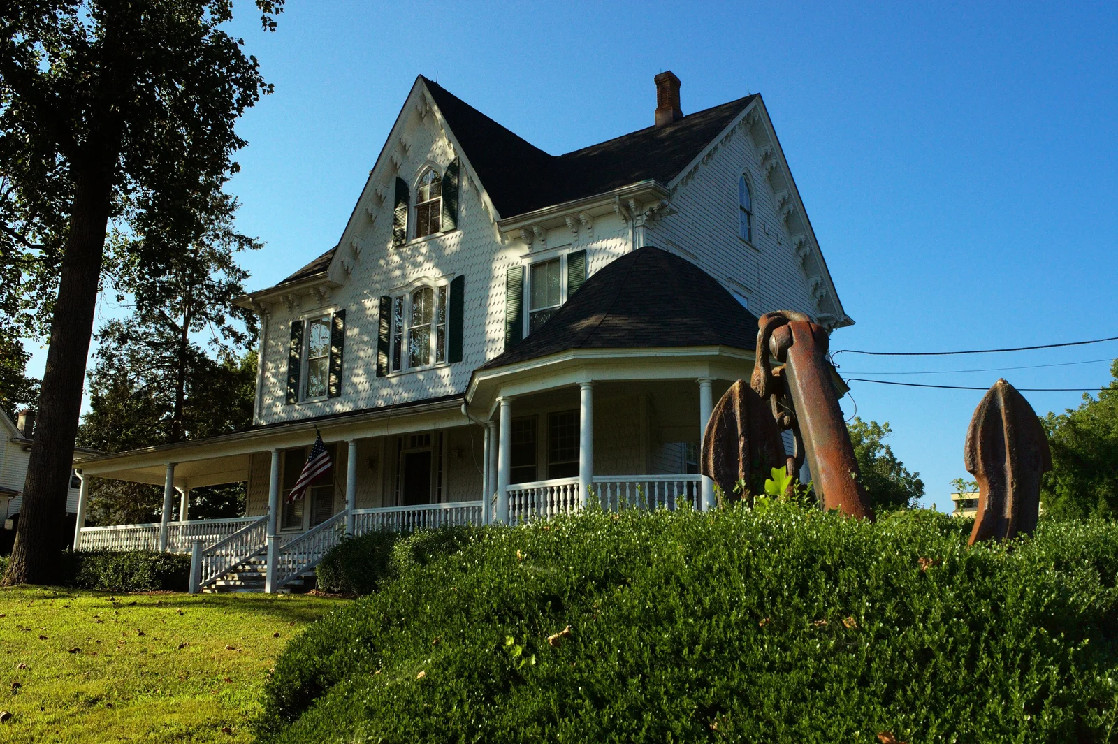White Victorian house with a wraparound porch and two large iron anchors on the lawn
