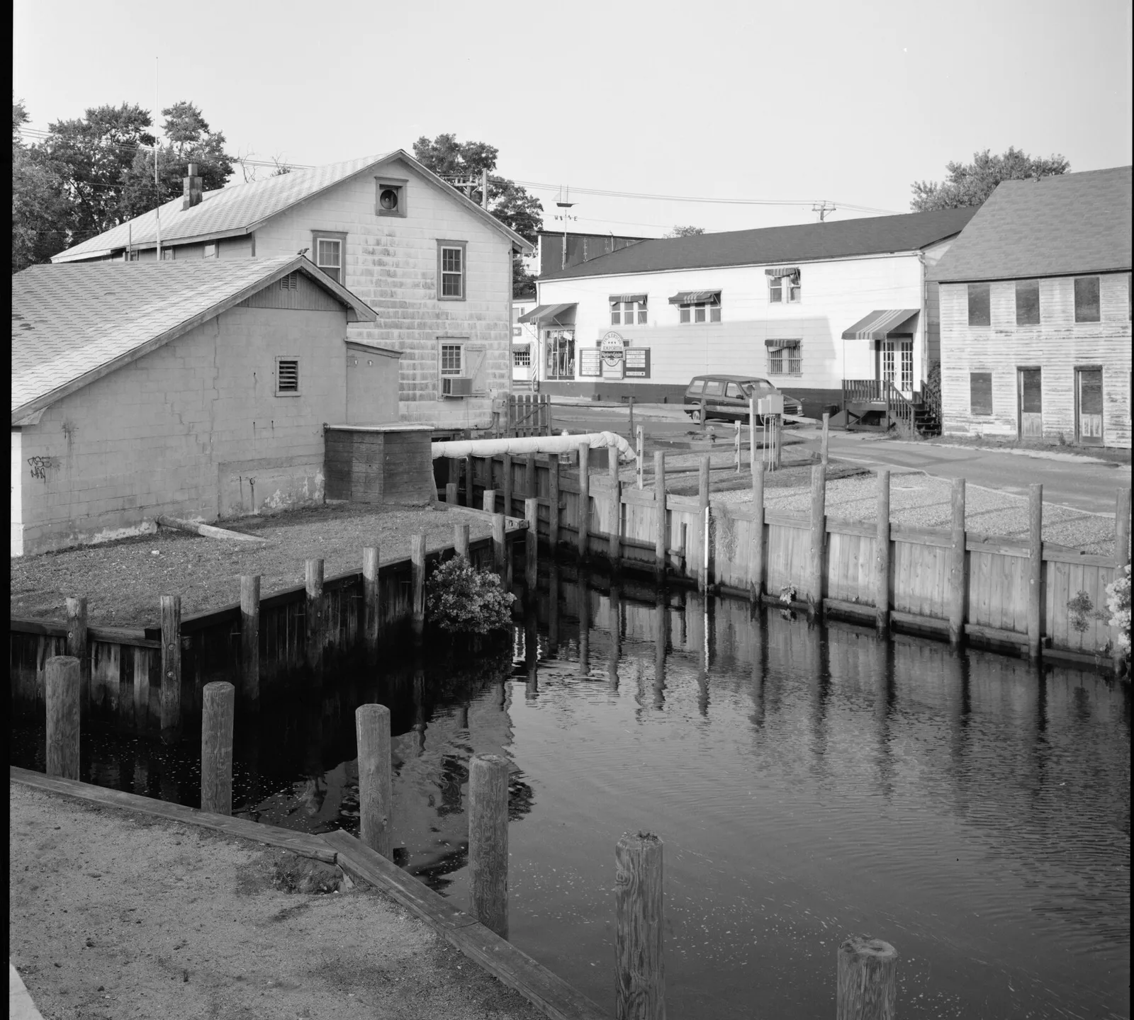 Old wooden buildings and bulkheads along Tuckerton Creek at the historic mill site, in black and white