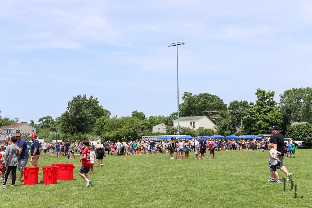 Crowds of families playing lawn games on the soccer fields, with a row of blue vendor tents along the far side