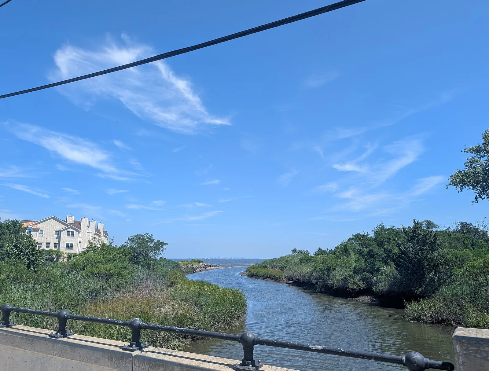 Flat Creek winding through green marsh toward the bay under a blue sky, with a house on the far bank