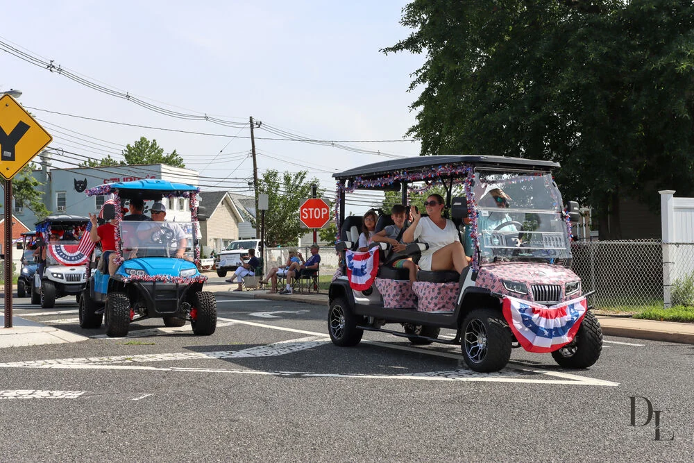 Golf carts decorated with red, white and blue bunting and pink trim driving in the parade