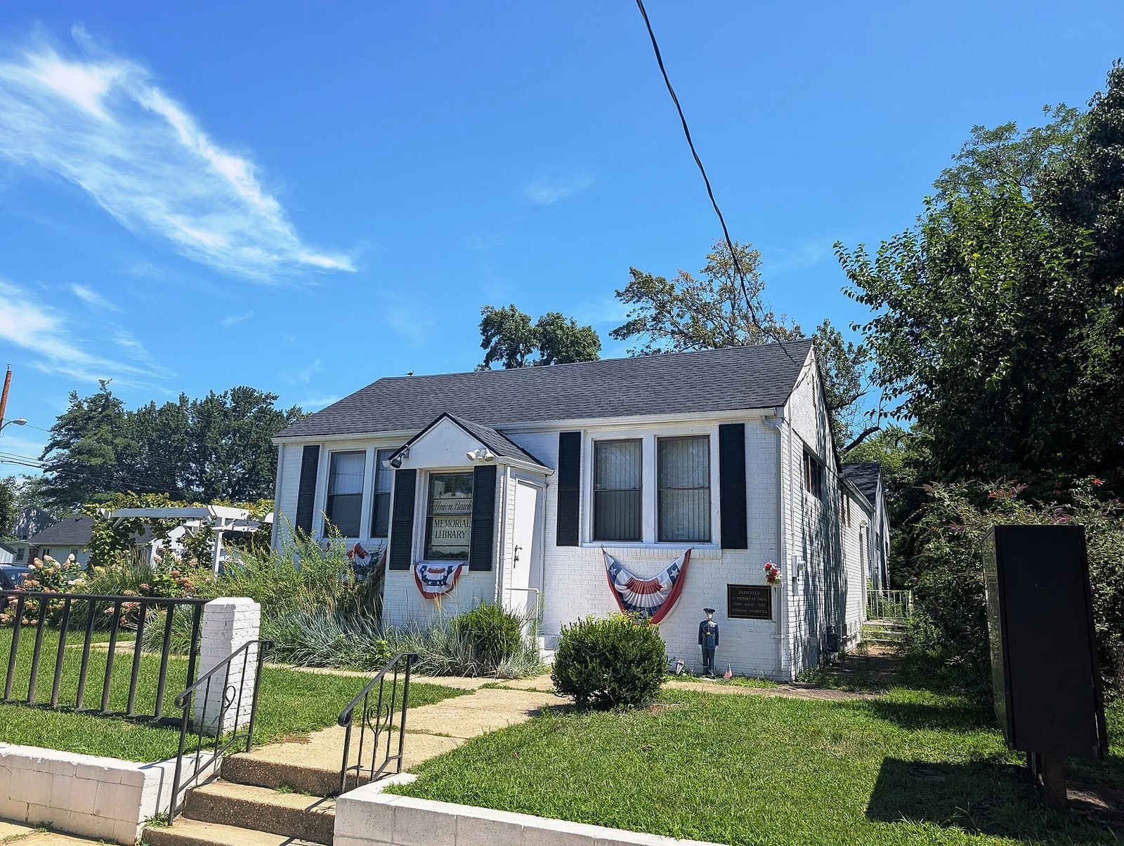 The Union Beach Memorial Library, a small white cottage with black shutters and patriotic bunting, set on a green lawn