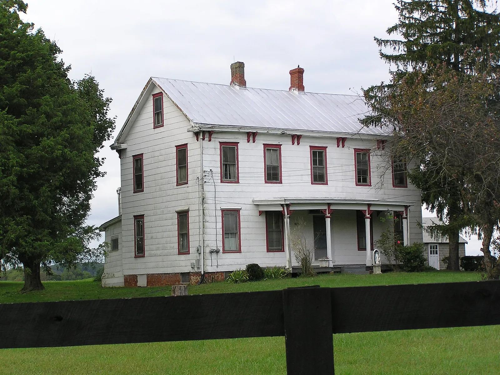 White two-story farmhouse with red trim behind a dark rail fence