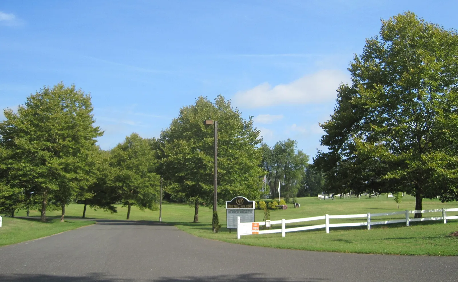 Tree-lined drive and white rail fences at the entrance to a horse show grounds