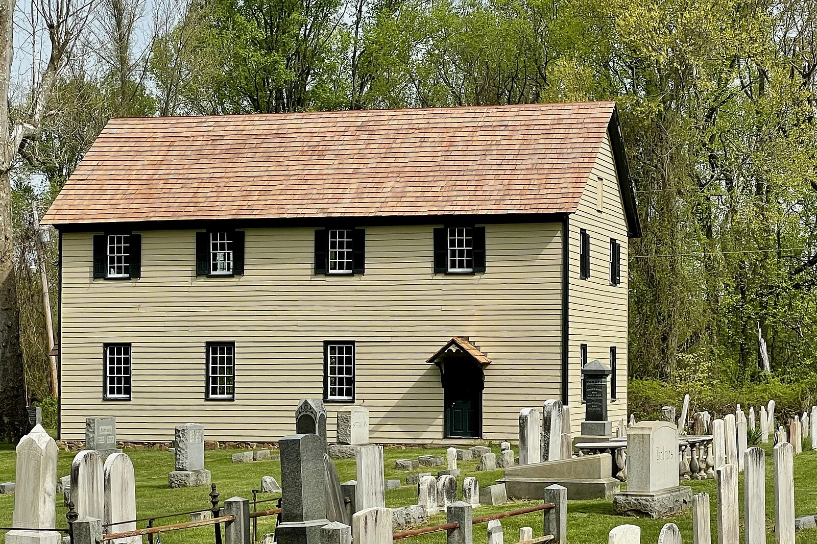 The two-story clapboard Yellow Meeting House with rows of weathered gravestones in the cemetery in front