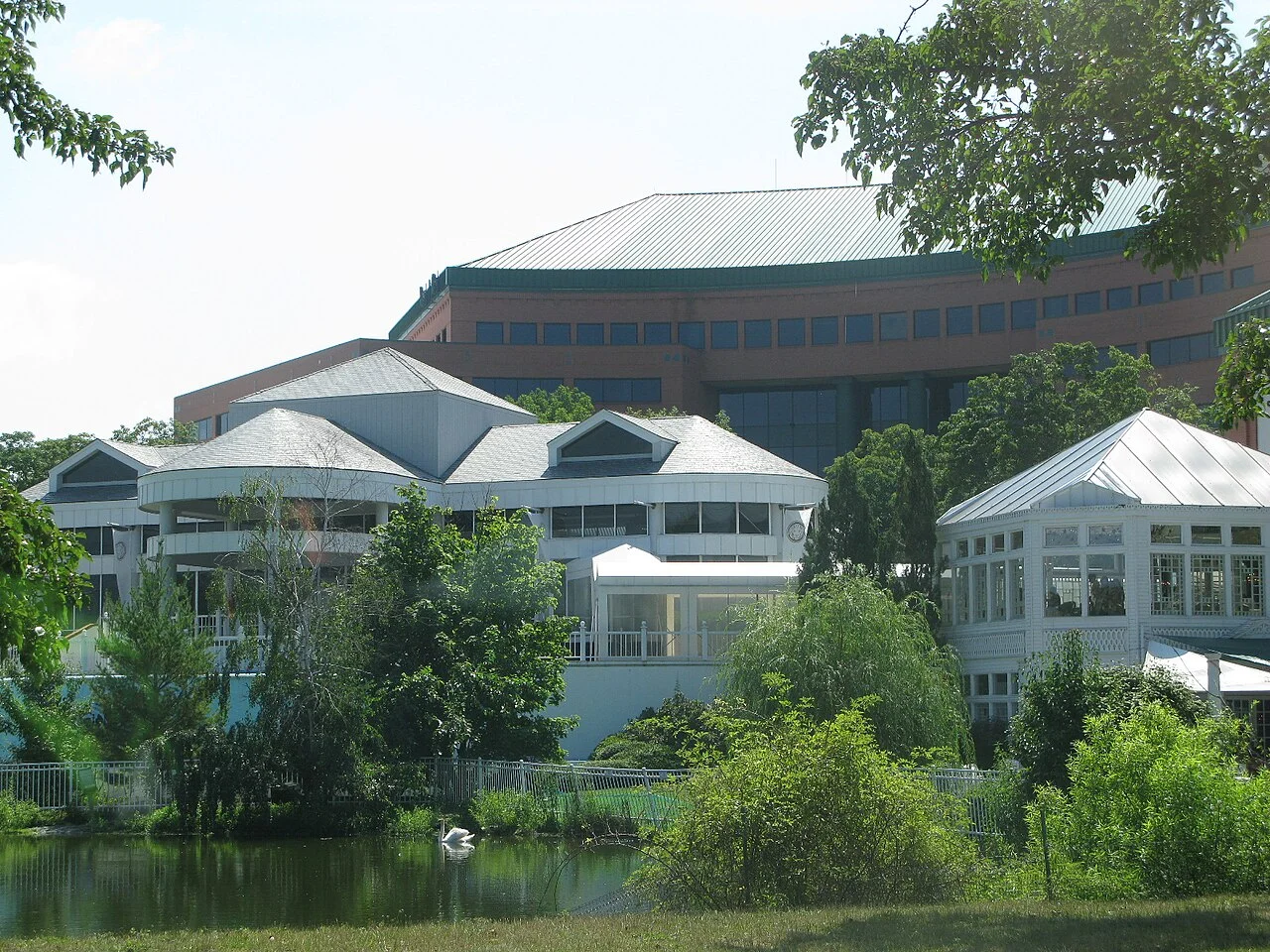 White-roofed buildings of the Main Street complex in Voorhees beside a pond with trees and shrubs