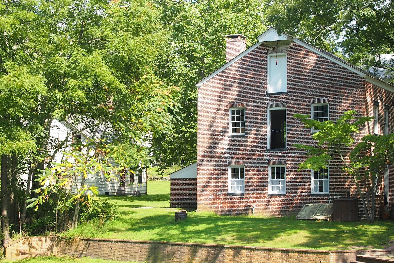 The red brick bakery building and the manager's house among shade trees in the Historic Village at Allaire