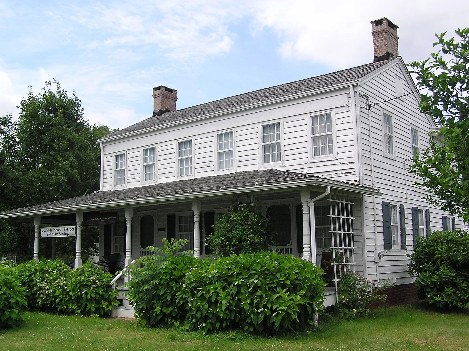 The white two-story Allgor-Barkalow Homestead farmhouse with a long front porch and shrubs along the lawn