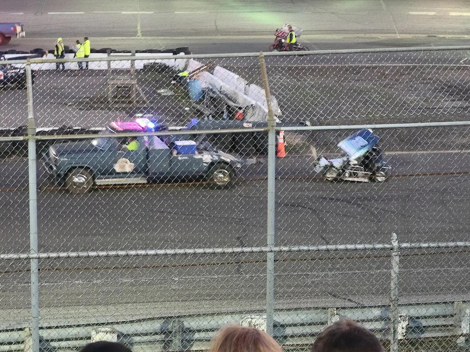 Race cars on the track at Wall Stadium, seen through the fence from the grandstand