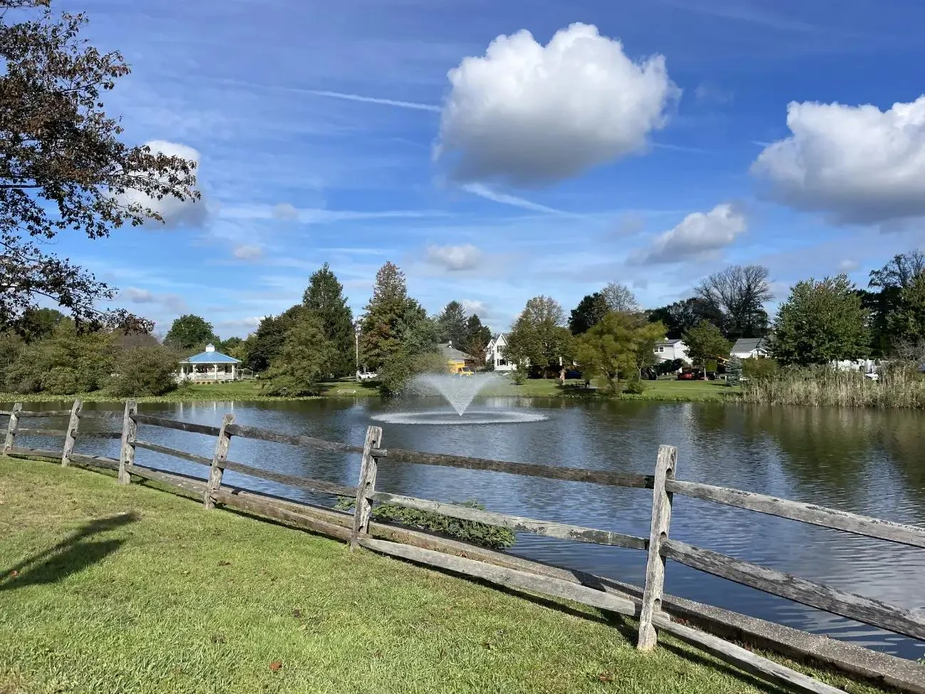 Franklin Lake with its center fountain spraying, a split-rail fence along the grassy bank and trees on the far shore