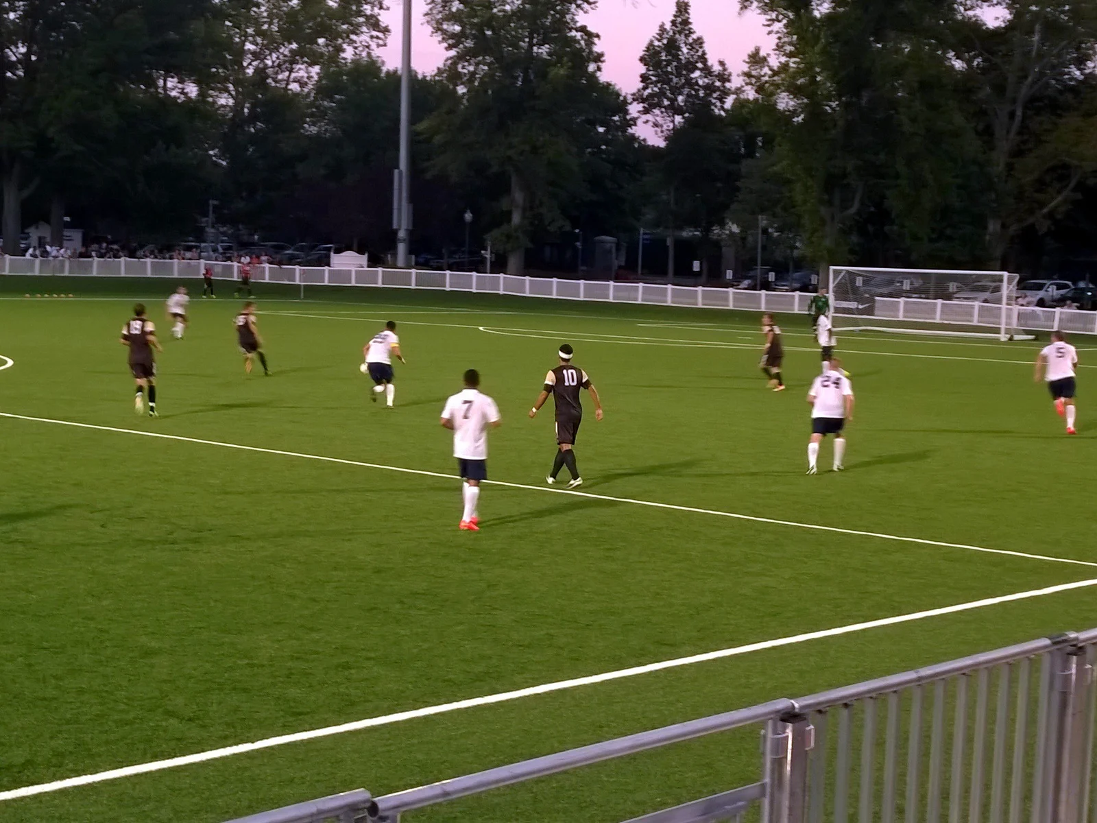 Players in white and dark uniforms running upfield during an evening Monmouth University soccer game
