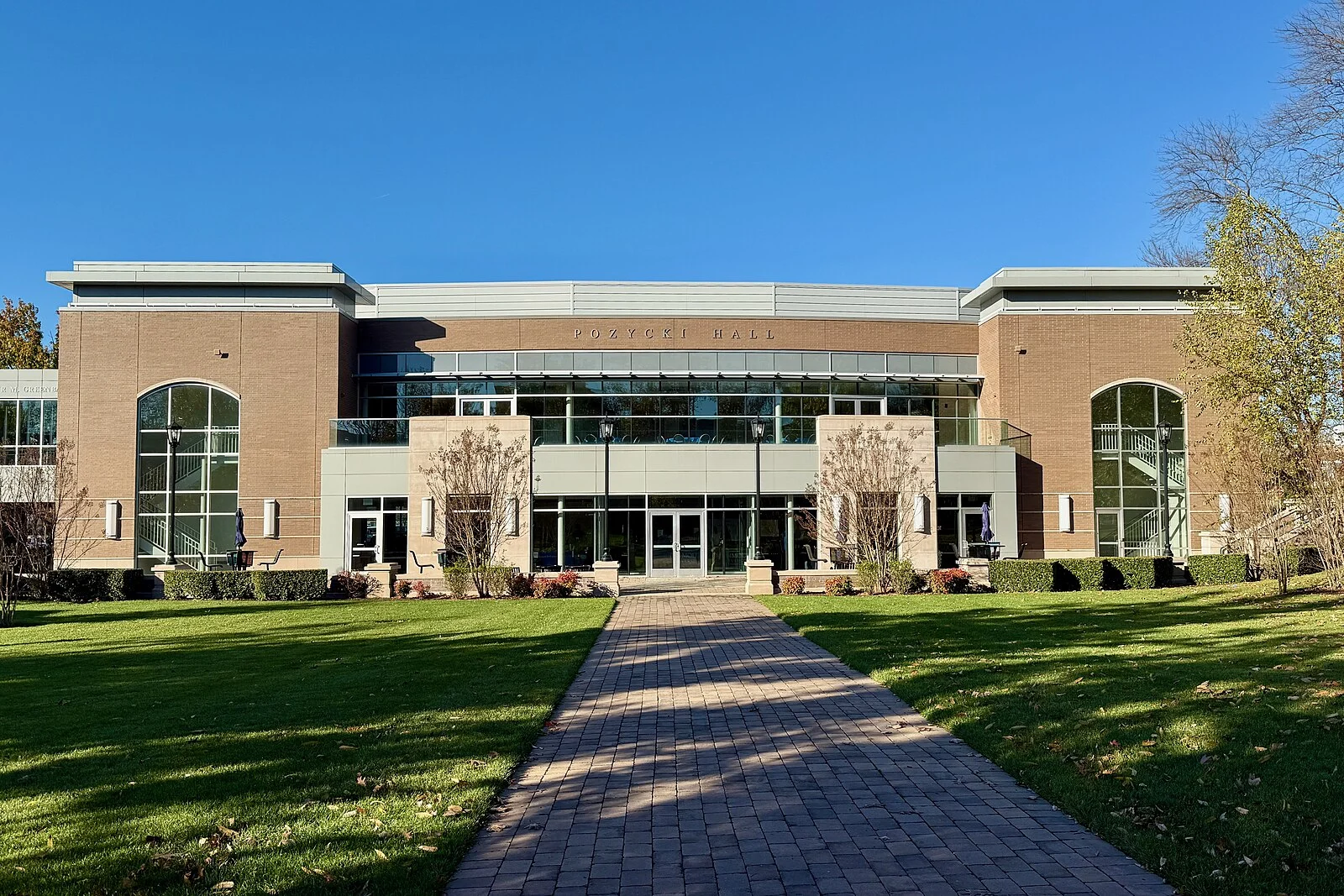 Brick Pozycki Hall with tall arched windows at the end of a brick walk across a green lawn