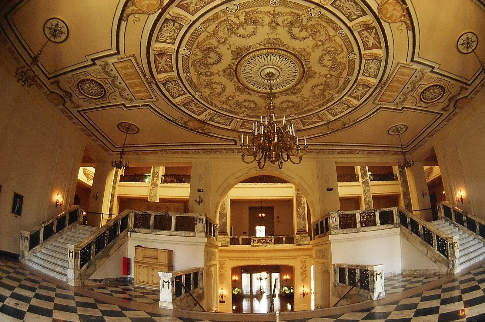 The ornate great hall inside Woodrow Wilson Hall, with a gilded ceiling, chandelier and twin staircases