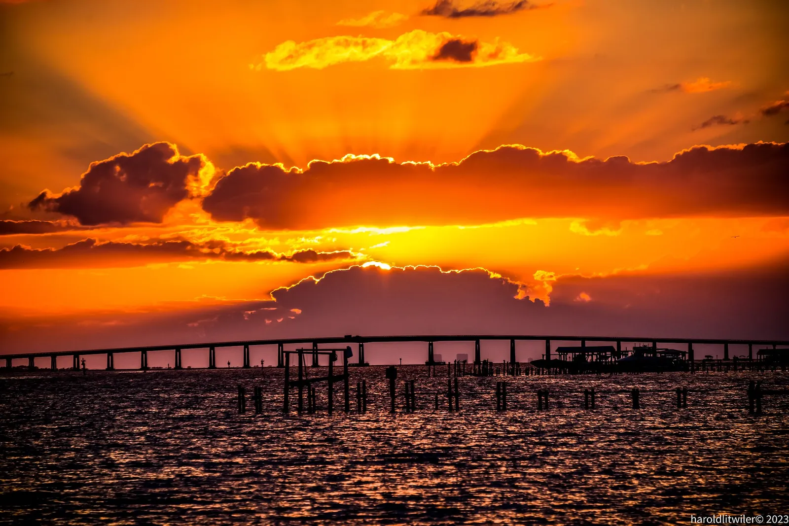 Orange sunset with sun rays over water and a long low bridge