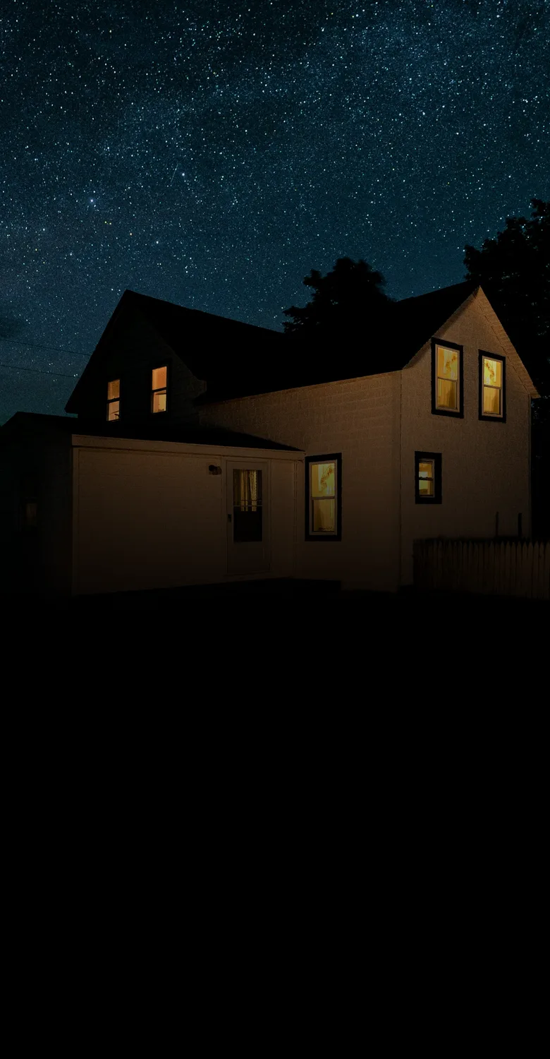 A farmhouse with lit windows under a starry night sky, fading into a fine-line drawing of a winding road with a fork and a red signpost, leading to a home