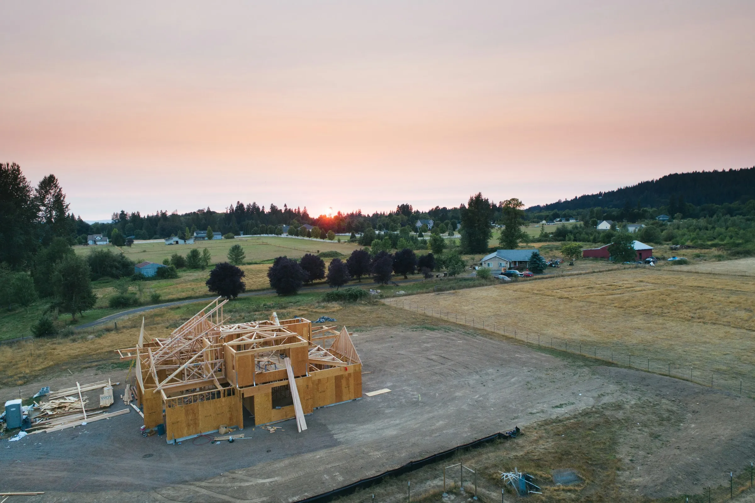The wooden frame of a new house under construction in an open field at sunset