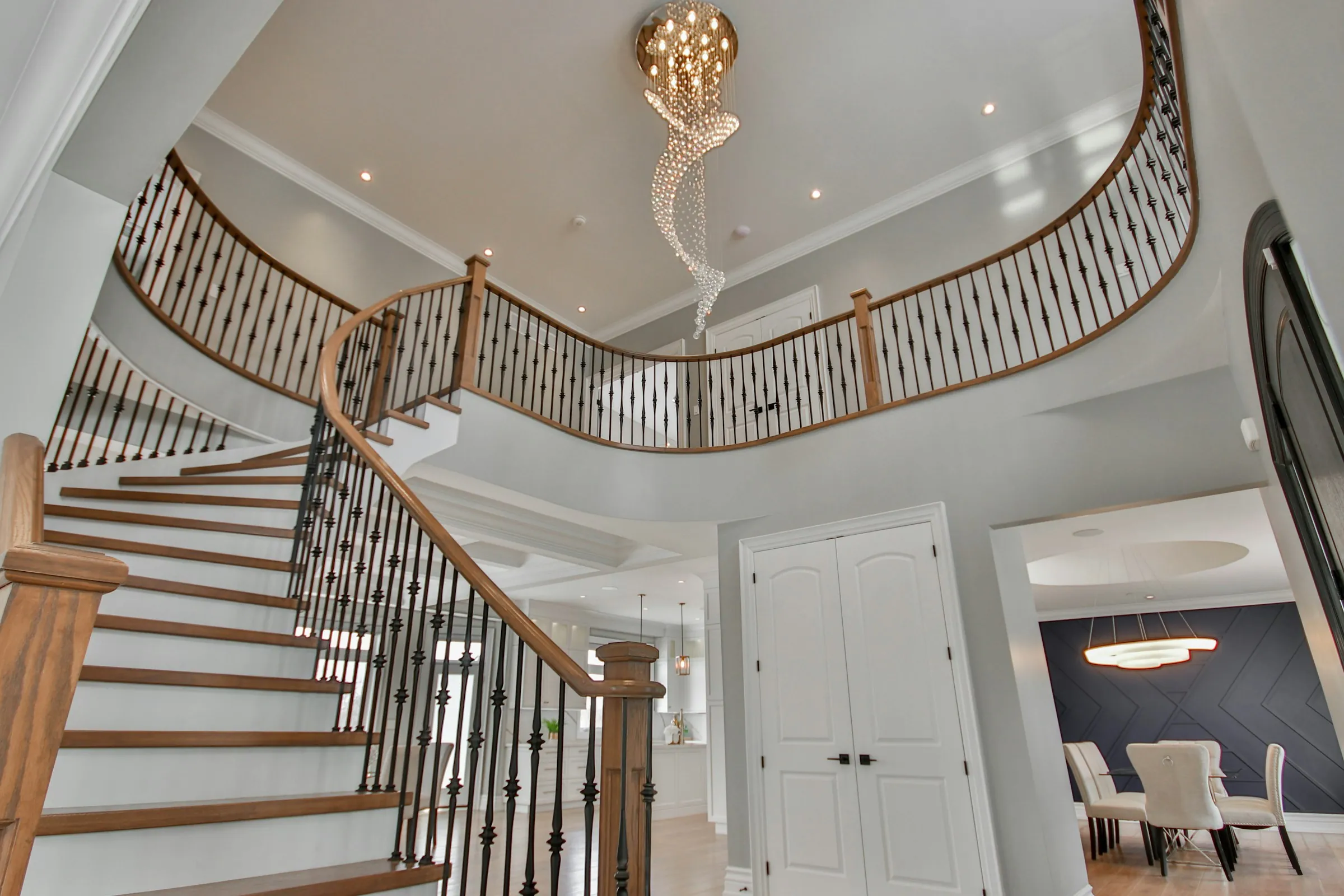 A curved staircase with dark iron railings under a crystal chandelier in a two-story entry hall