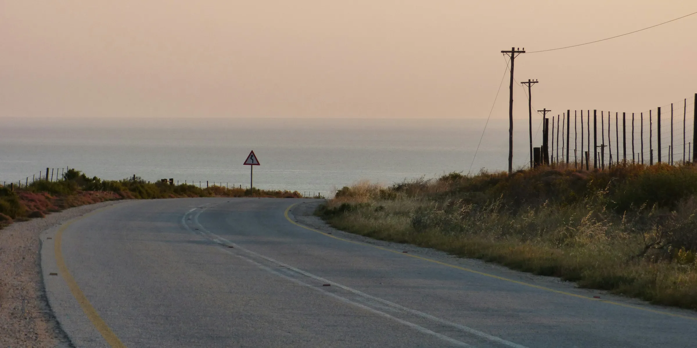 Winding two-lane road leading toward the ocean under a soft evening sky