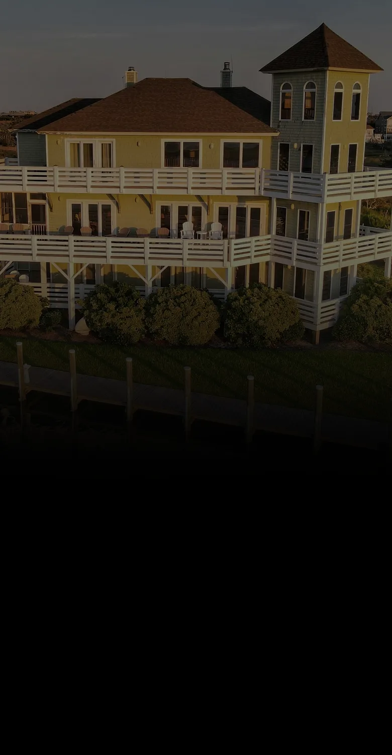 Coastal home with wraparound decks behind a wooden bulkhead and dock at golden hour, beside a line drawing of a raised lagoon home, its dock and a boat