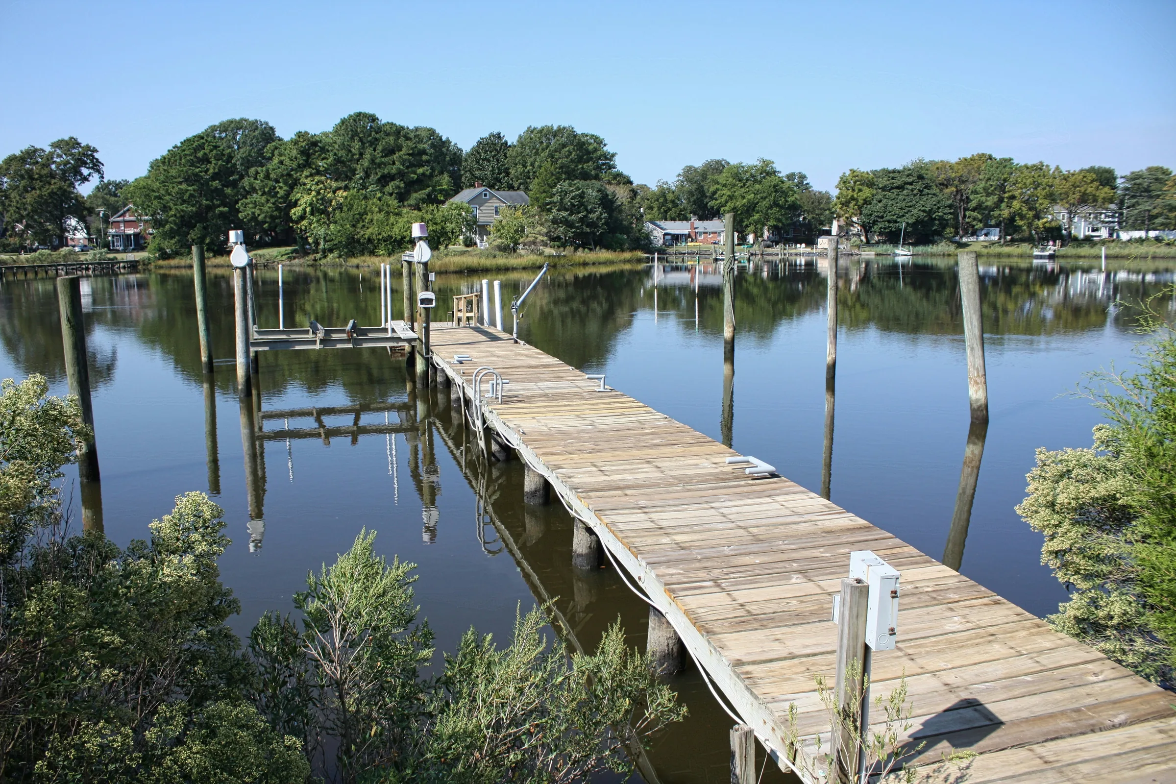 Long wooden dock on pilings with a boat lift, reaching across calm water