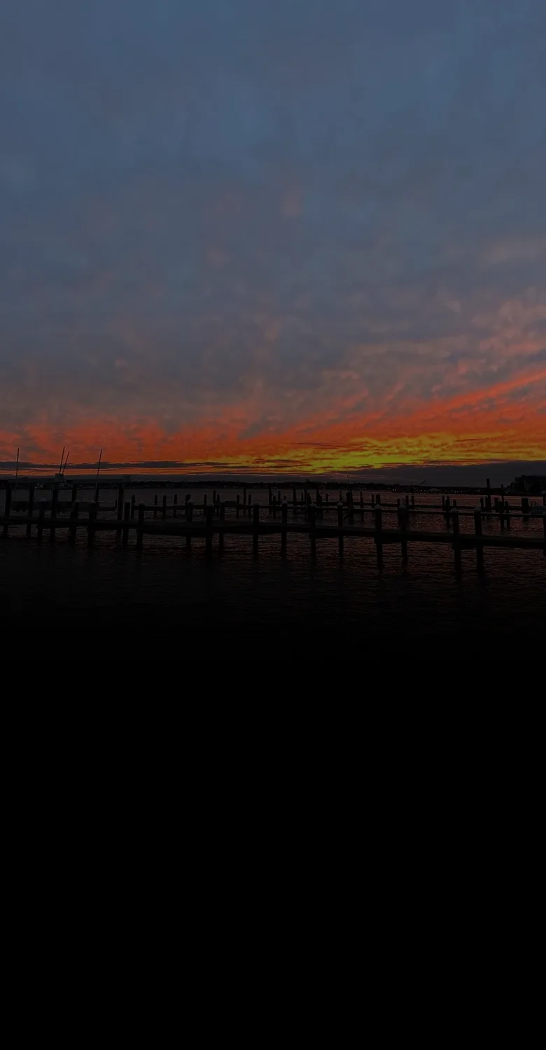 Docks on the Metedeconk River at sunset, fading into a fine-line drawing of a lighthouse and a shore home